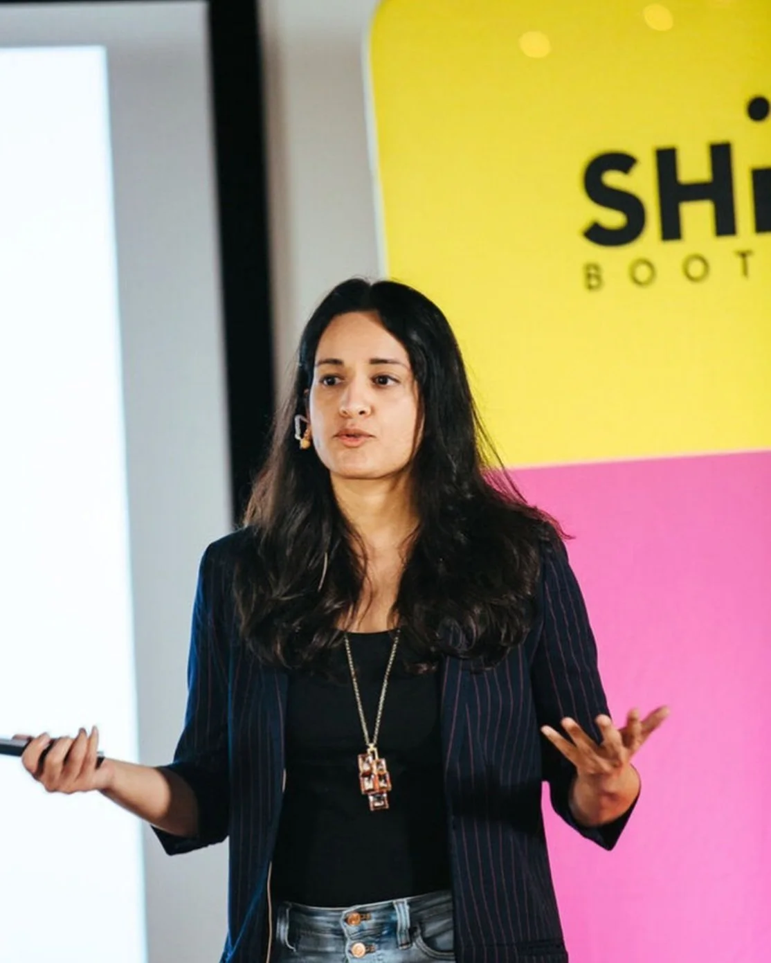 A Shine speaker presenting in front of a pink and yellow Shine Bootcamp backdrop